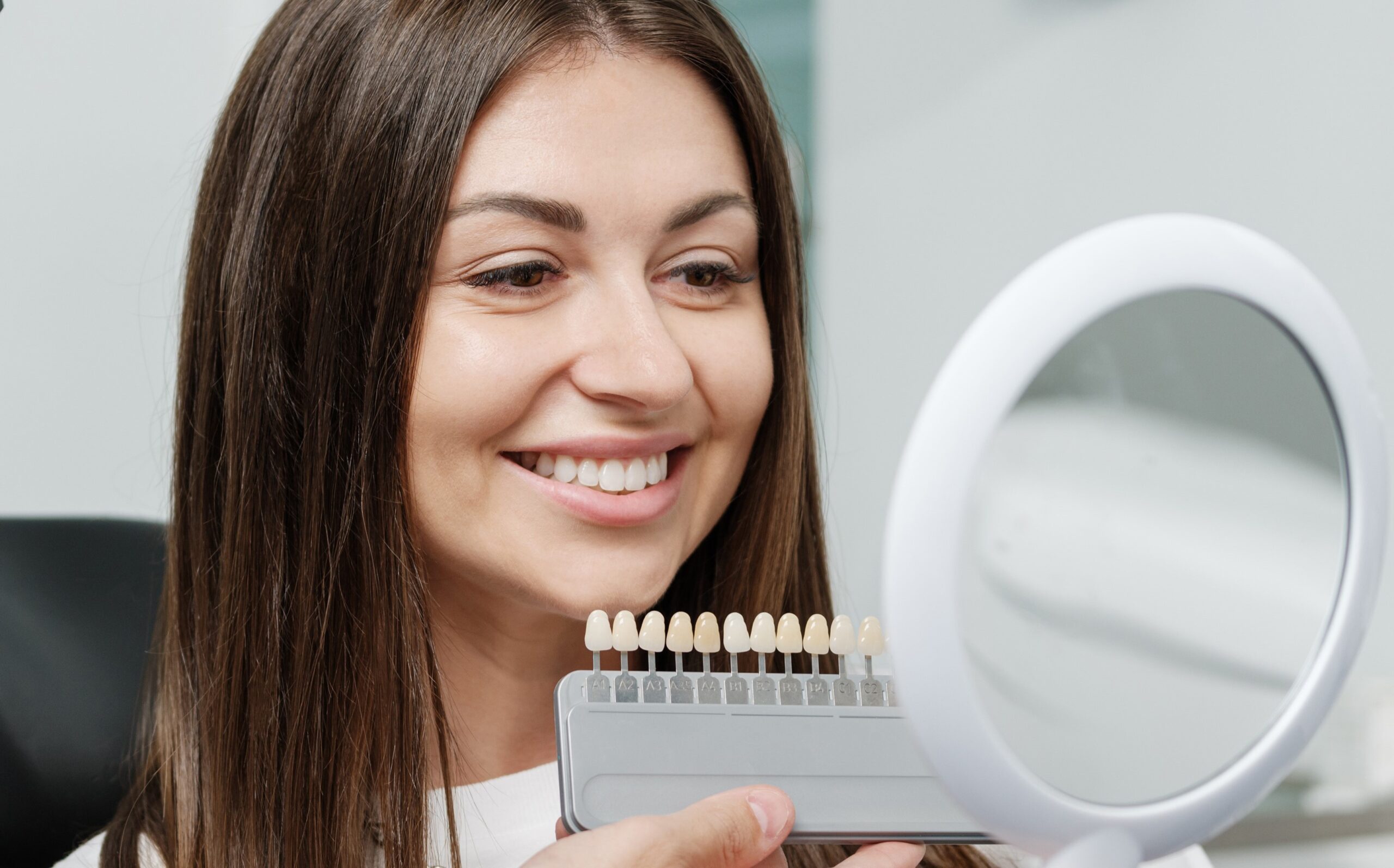 Young man dentist in white coat show veneers enamel color palette for beautiful patient woman