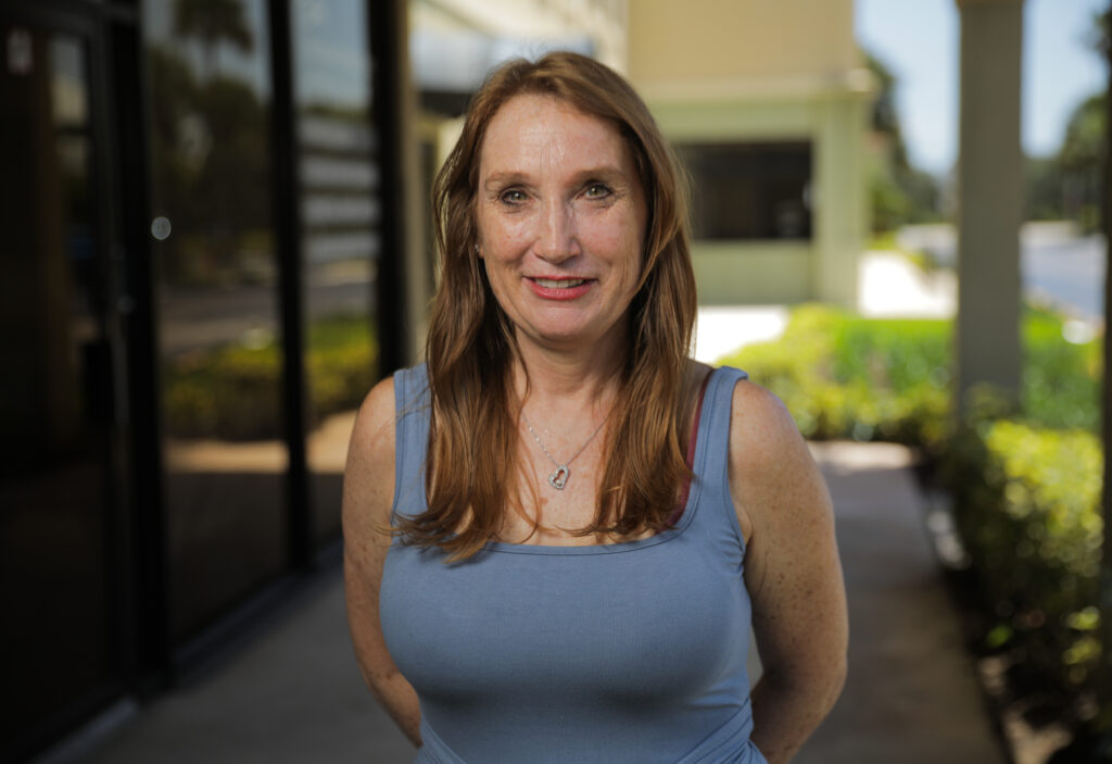 Woman with long brown hair smiling at camera outdoors in front of dental office building